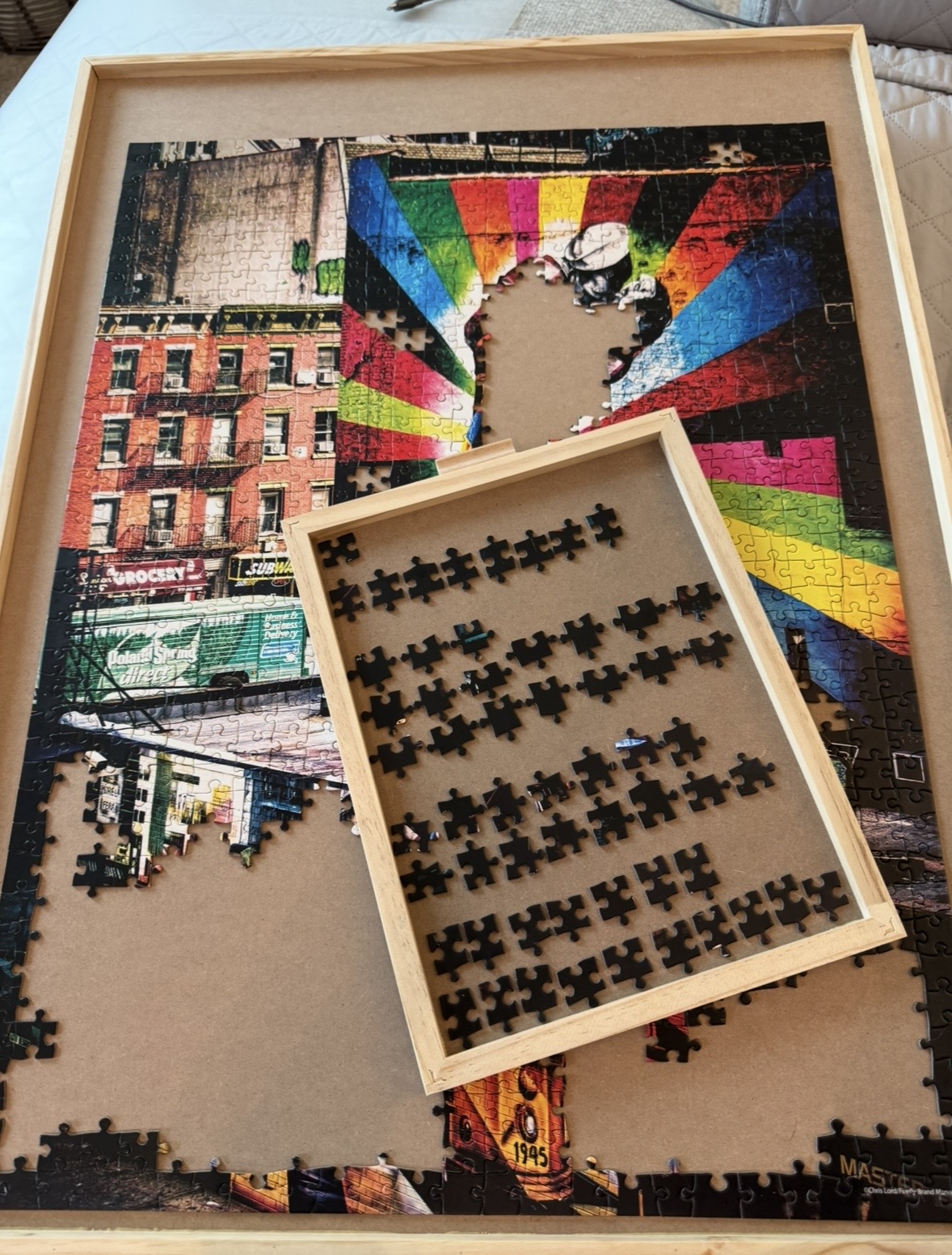 A 1,000 piece puzzle in progress inside a wooden frame, with a sorting tray of pieces on top.