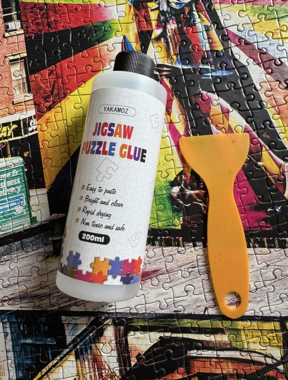 A bottle of jigsaw puzzle glue and an orange spreader resting on a finished puzzle.